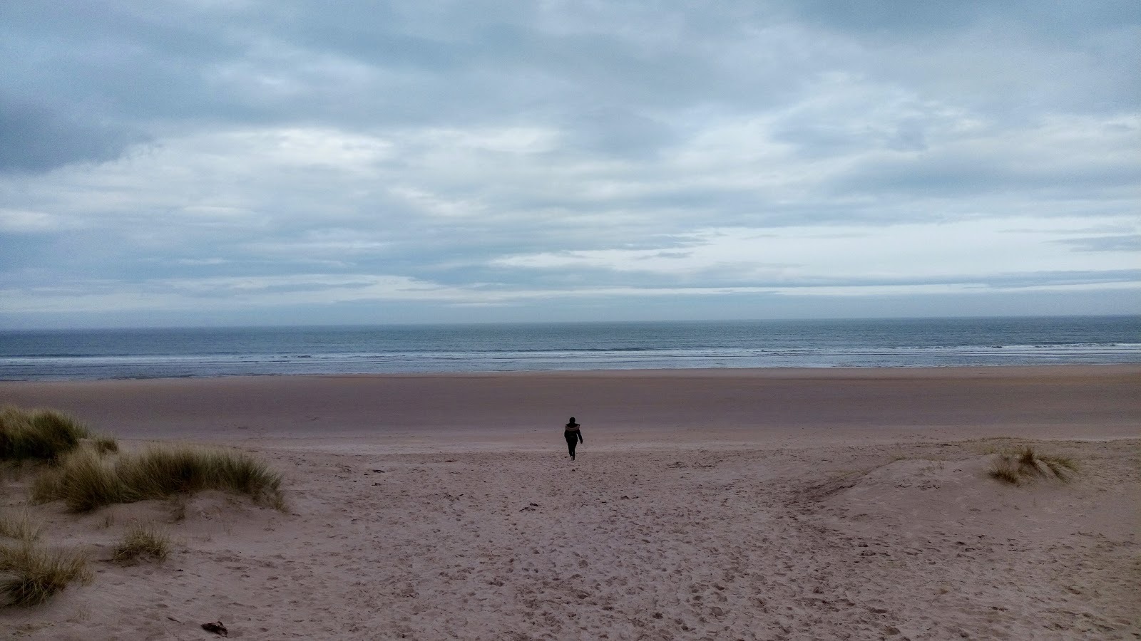 Lone woman walking on Ross Sands beach towards the sea.