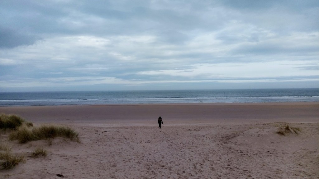 Lone woman walking on Ross Sands beach towards the sea.